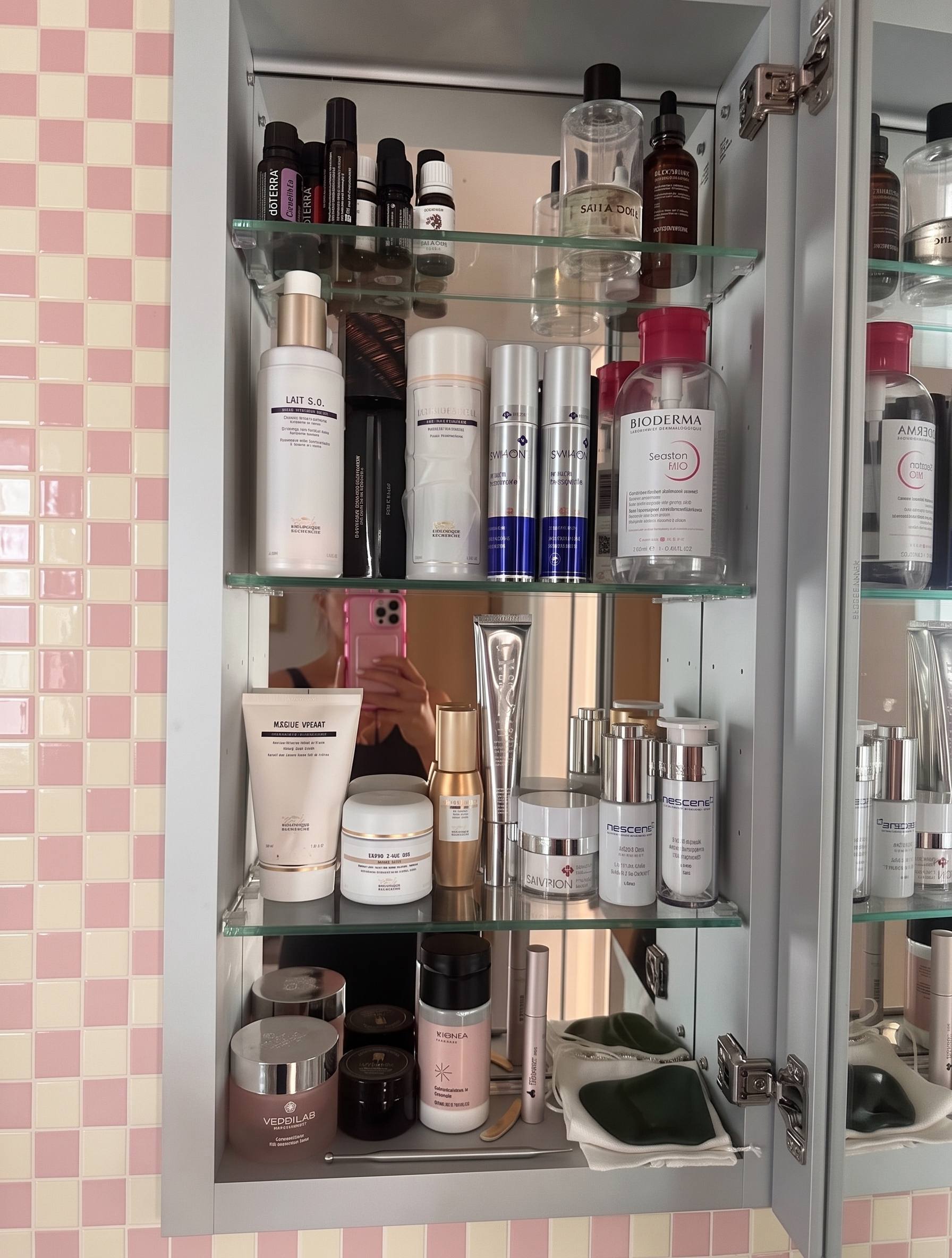 A mirrored bathroom cabinet in Switzerland: dōTERRA oils on the top shelf, Biologique Recherche and Bioderma in the middle, Nescens and Verdilab below