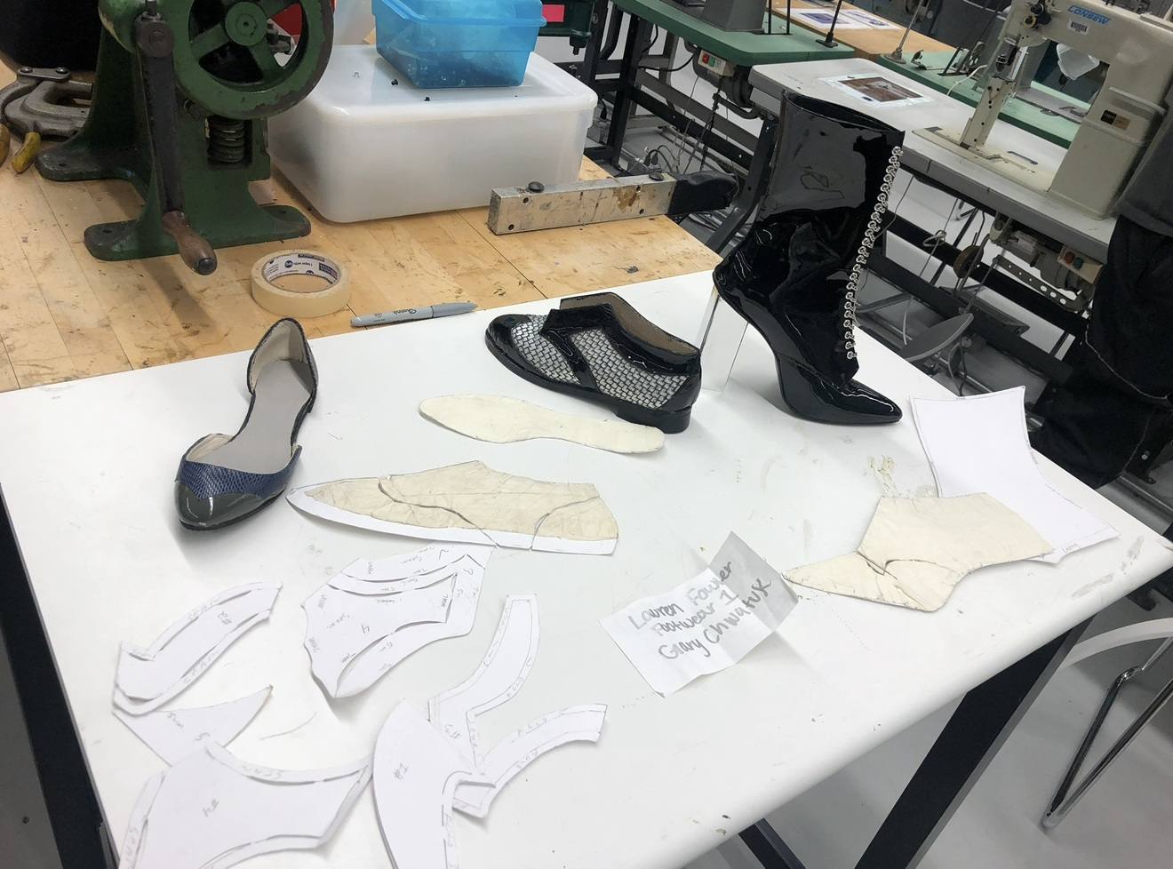 A shoe factory bench — paper patterns, a sample flat and a patent boot beside industrial machines