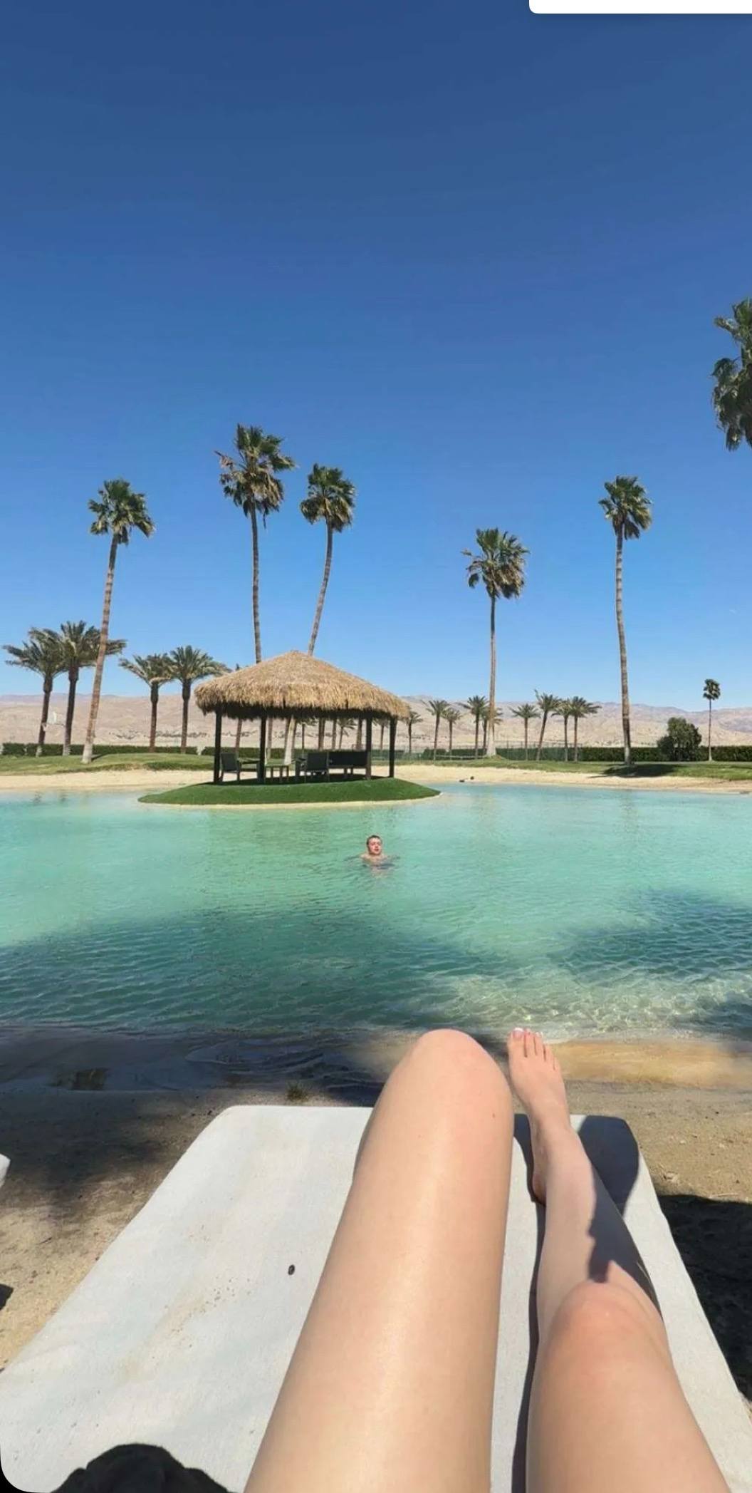 Legs stretched out beside a desert lagoon lined with palms