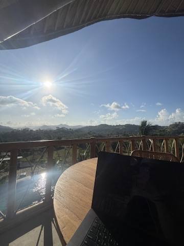 A laptop on a timber deck with the sun flaring over the railing