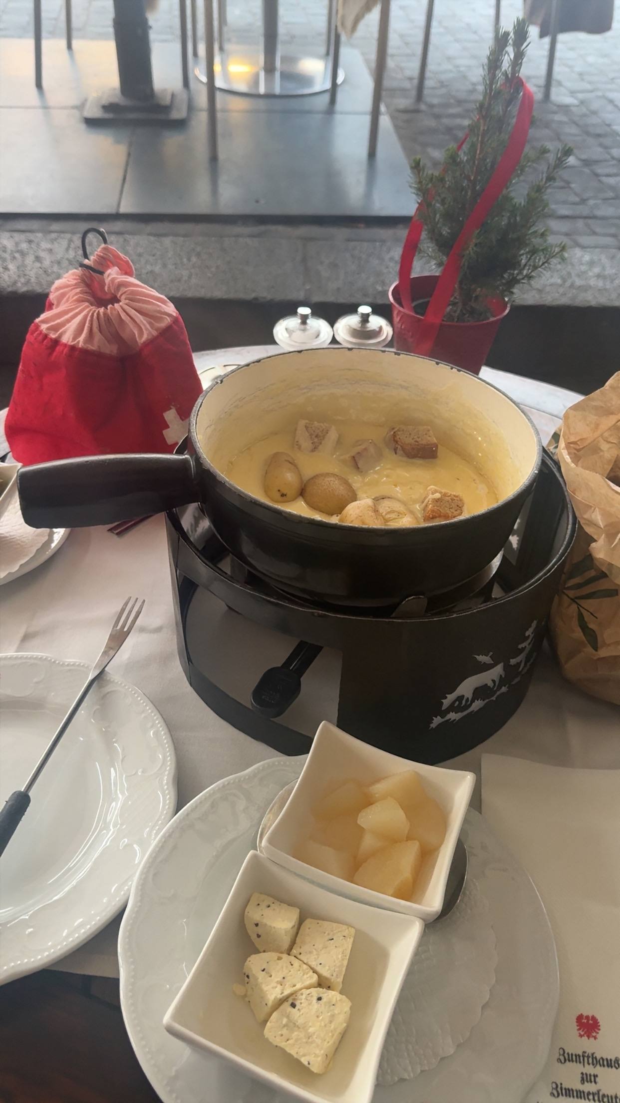 A fondue pot on the table with bread and pickles