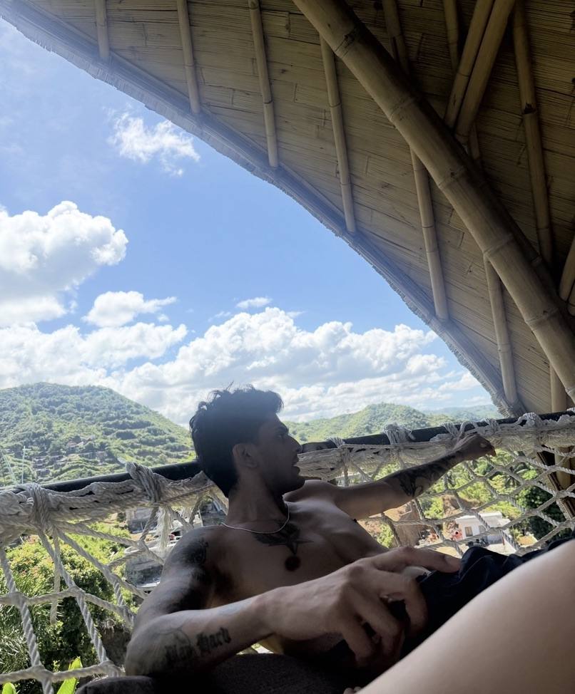 Lying in a hammock under a timber roof looking out at the hills
