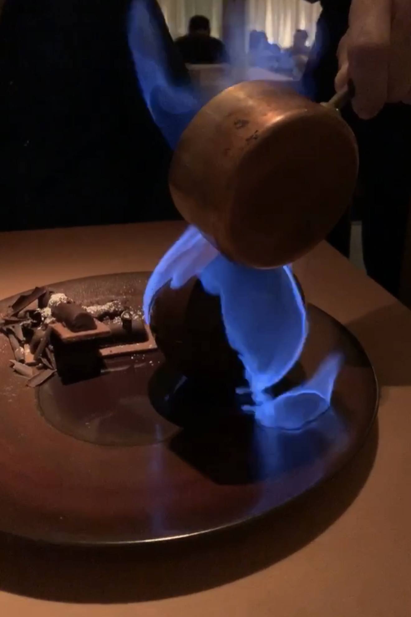 A copper pan flambéd at the table, blue flame over dessert