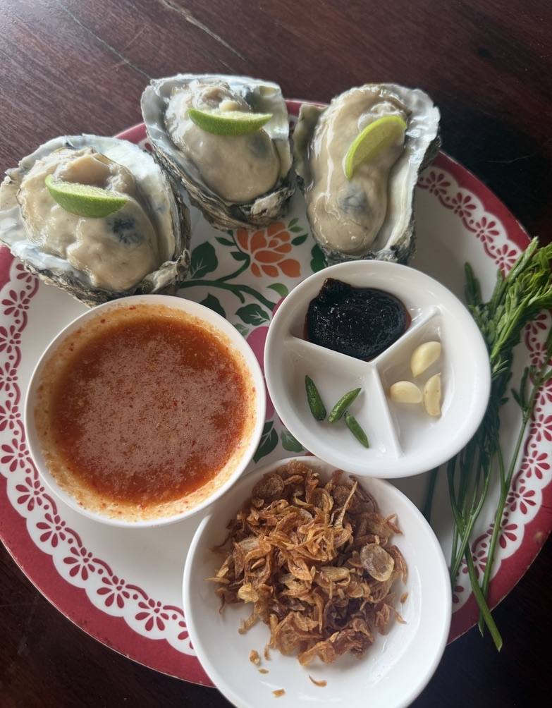 Oysters, chilli sauce and garnishes on a patterned plate