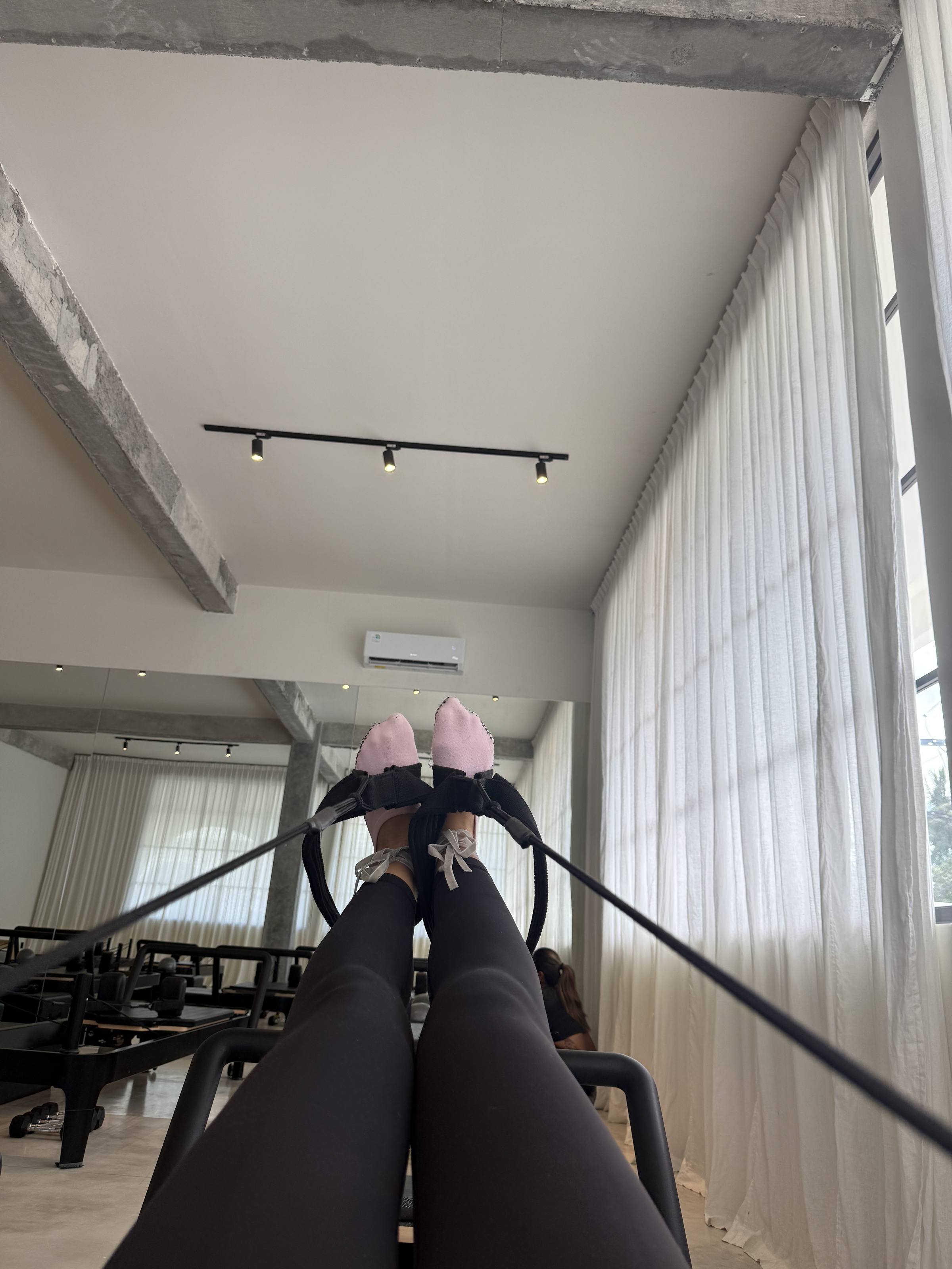 Feet in grip socks in the reformer straps, light through the curtains