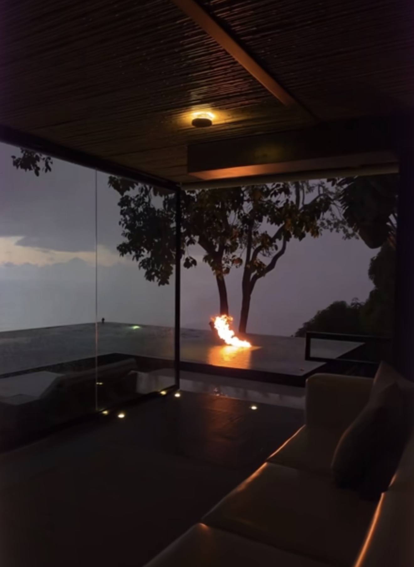 Fire trough burning beside an infinity pool at dusk under a timber ceiling