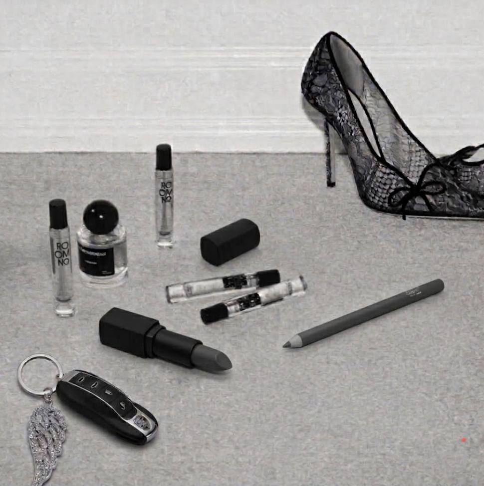 Grey flatlay of fragrance vials, a black lipstick, car key and a lace pump