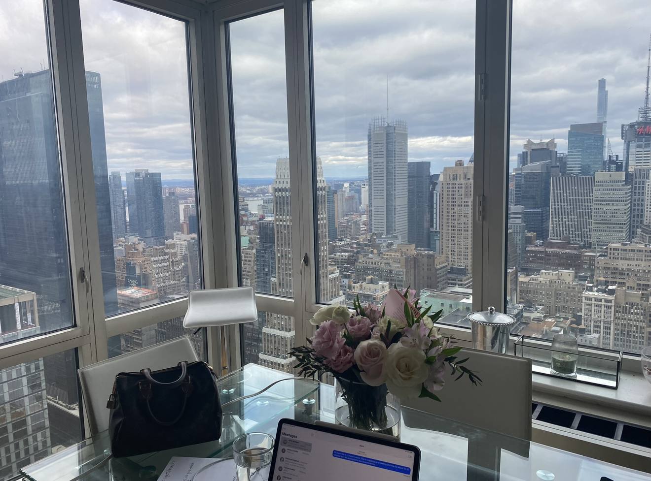 Glass desk with roses, a laptop and a handbag in front of a Midtown skyline